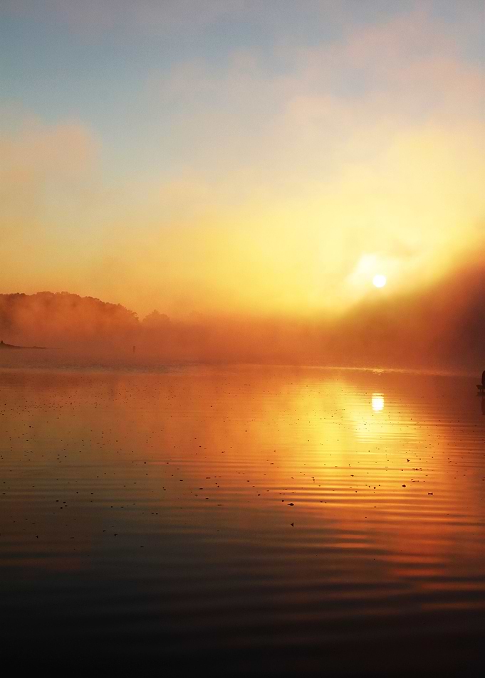 The sun rises through mist over a lake in the Appalachi ...