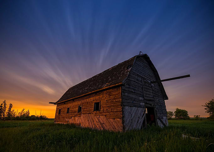 Abandoned barn at night with moving clouds and city lig ...
