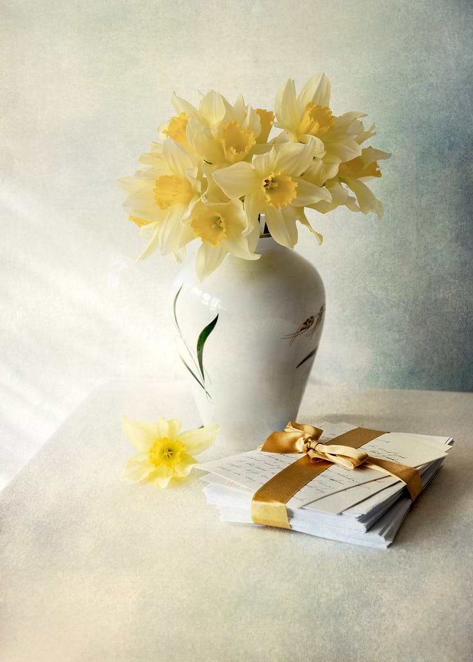 Still life with daffodils in the vase and pile of lette ...