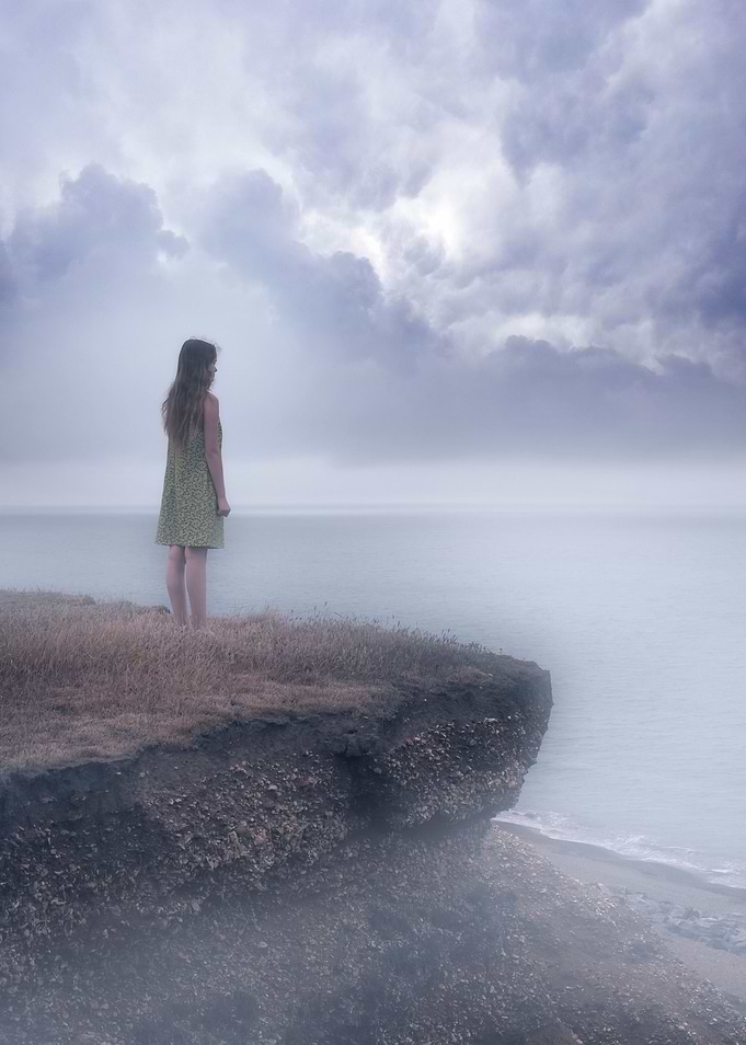 a girl standing on the edgle of a cliff over a foggy se ...