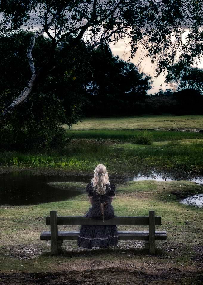 a blonde girl in a floral dressl is sitting on a bench ...
