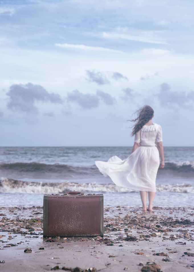 a woman is walking into the sea, leaving her luggage be ...