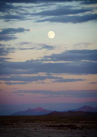 the moon rises over mountains in the desert.