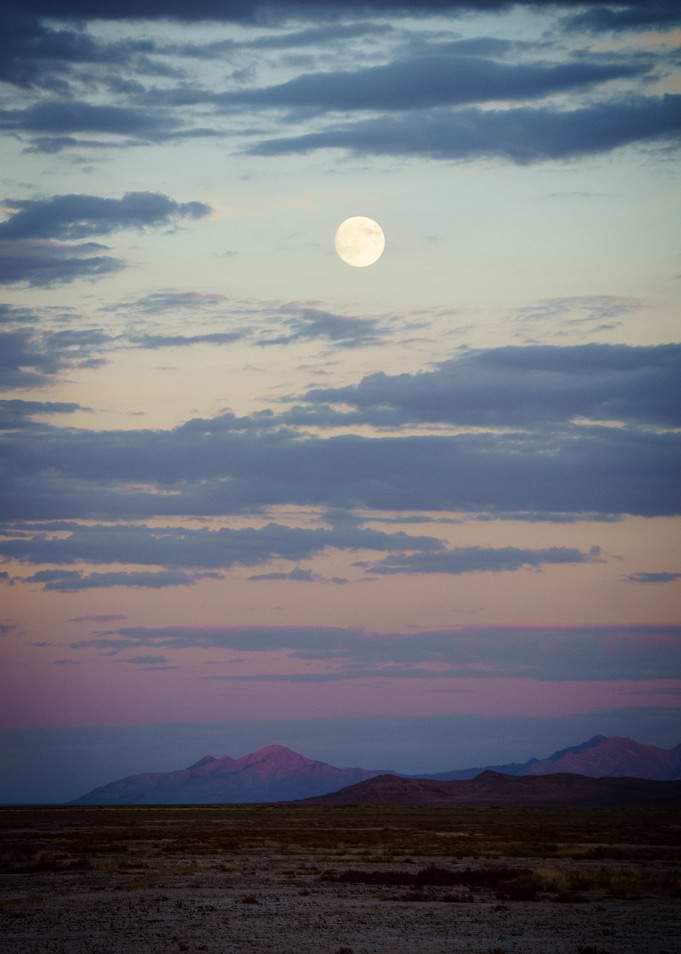 the moon rises over mountains in the desert.