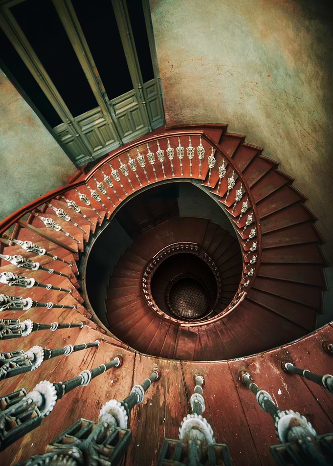 An old spiral staircase in red and brown tones.