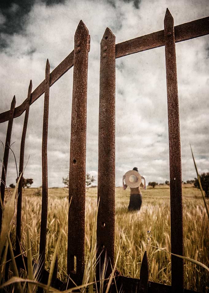 Rusty gate in a hay field with a woman wearing a big ha ...