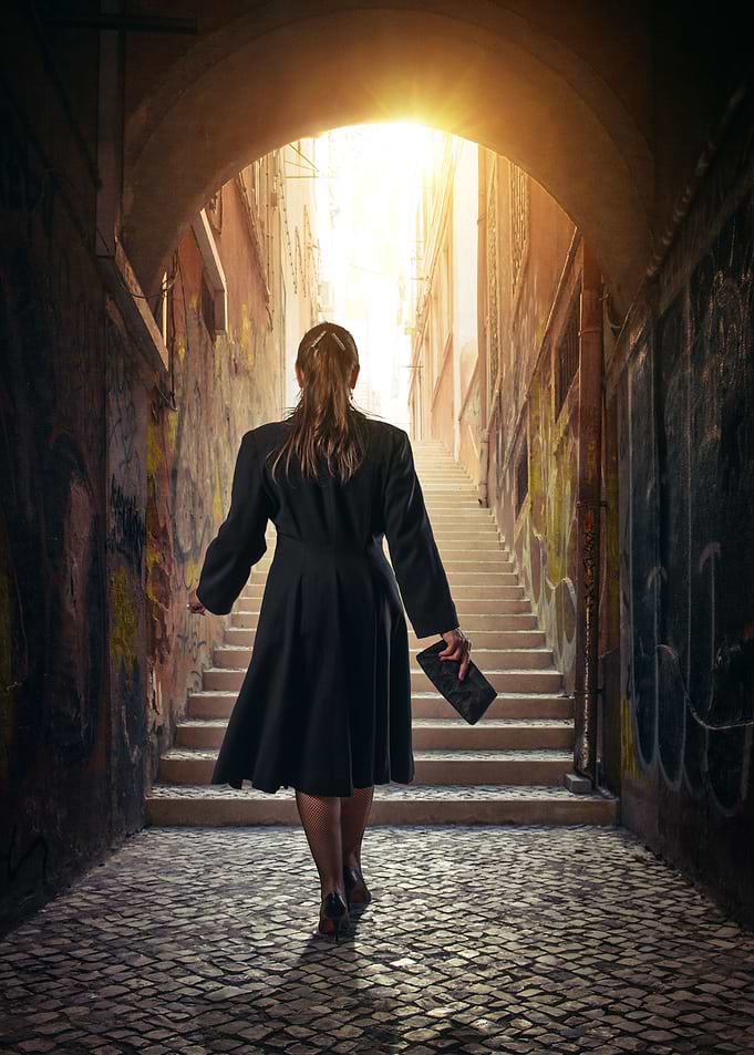 Woman in black dress walking up a stairway in a narrow ...