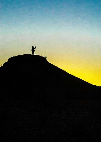 A photographer stands silhouetted on a hill as the dese ...