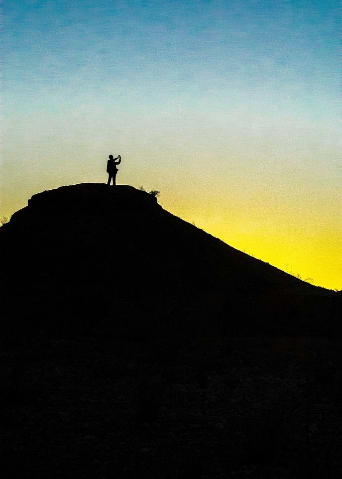 A photographer stands silhouetted on a hill as the dese ...