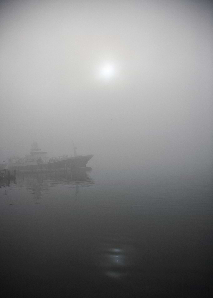 The sun peeking through the fog by the harbor in Tromsø ...