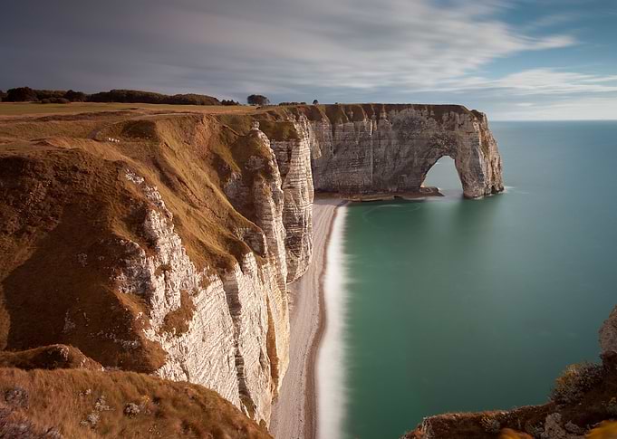 The Manneporte arch, pebbled beach and coastline of Etr ...