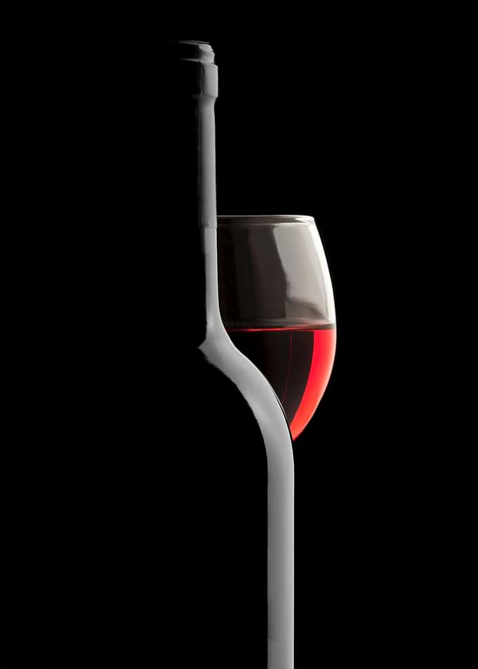 Elegant close-up photo of a wine bottle and wine glass with red wine on a black background. The glass is behind the bottle and has a rich intense red color. Bottle silhouette is made by the light reflection. Sophisticated composition for wine lovers.