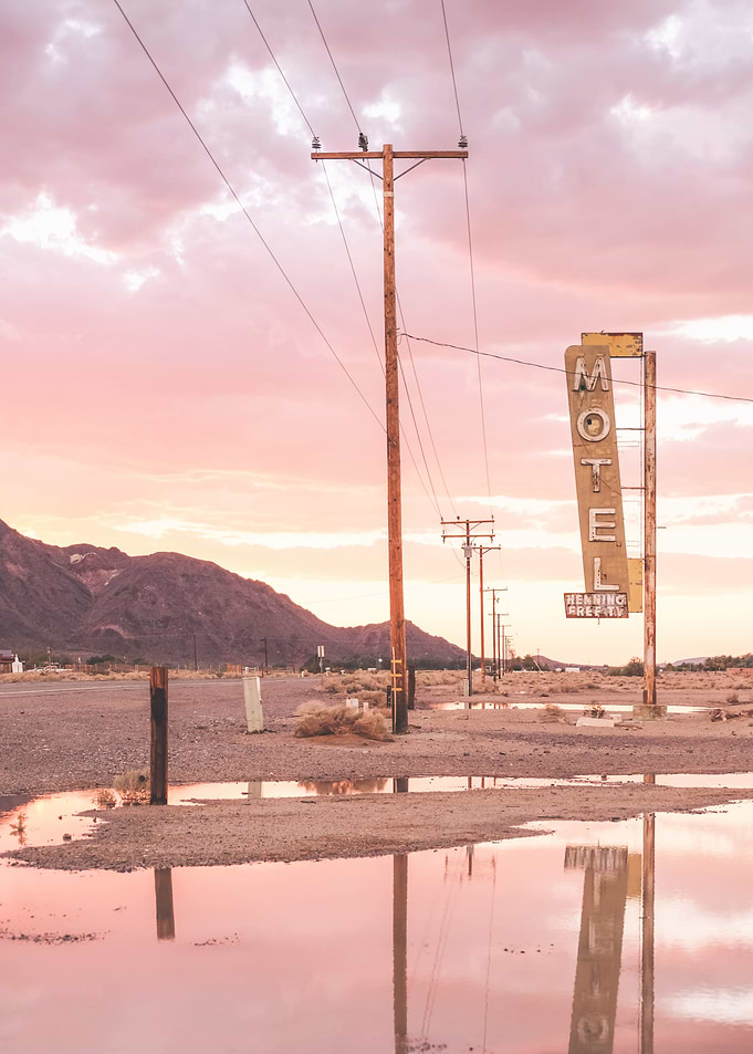 Route 66, USA I Sunset in front of a vintage retro motel neon sign in a California desert landscape to pastel pink sky sun aesthetic and a mirrored reflection in water in front of the Bagdad Cafe
