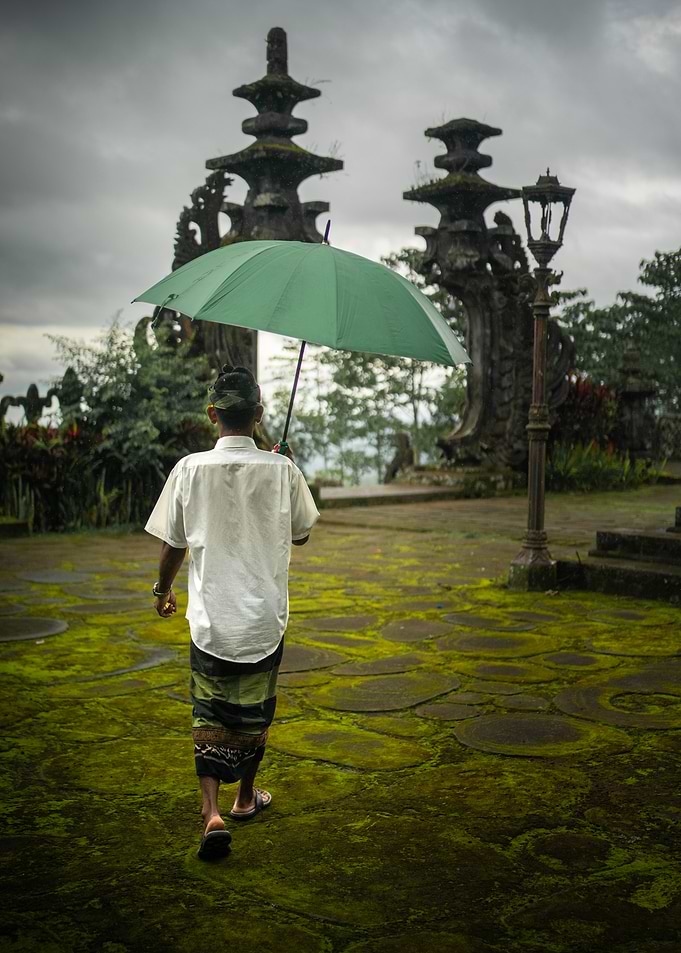 Balinese Man Walking Under Umbrella in Besakih temple