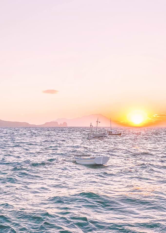 Milos, Greece I Summer pastel pink aesthetic sunset in the fishing village of Klima with its boats on the Mediterranean sea in the mountains of the wild boho nature on Cyclades islands like Santorini