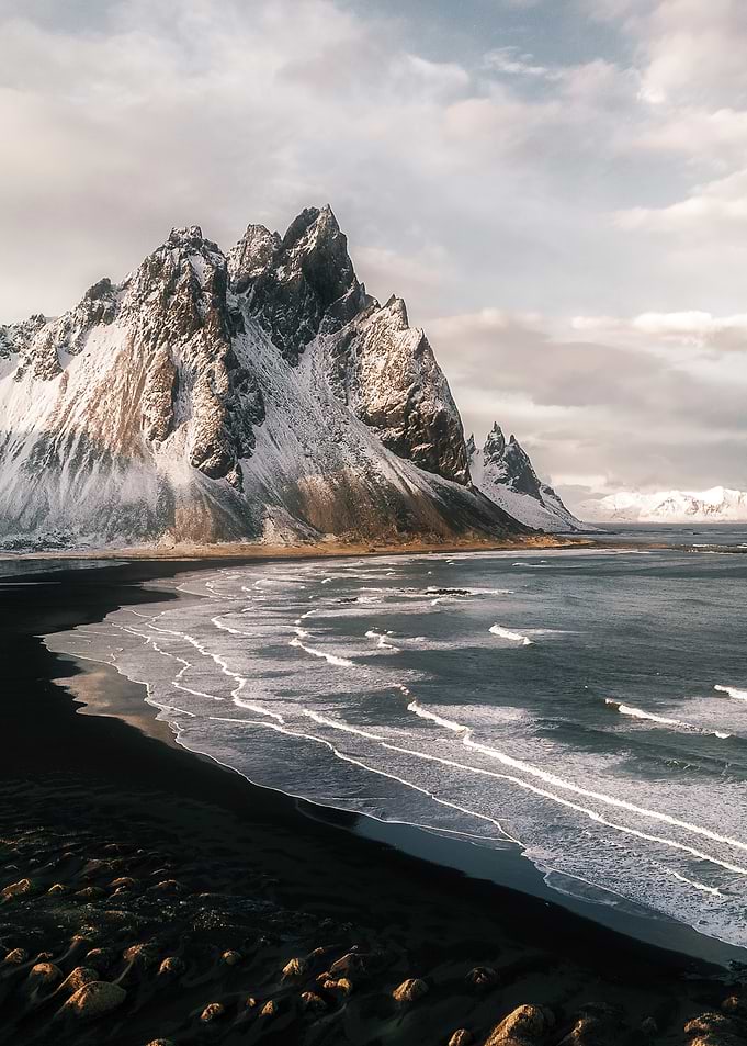 Snowy Mountain Range along the Icelandic Coast with black Sand Beach and Waves at Sunset