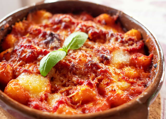 Gnocchi alla Sorrentina, Italian Potato Dumplings in Tomato Sauce, Gratinated With Mozzarella Cheese in a Terracotta Dish. Selective focus.