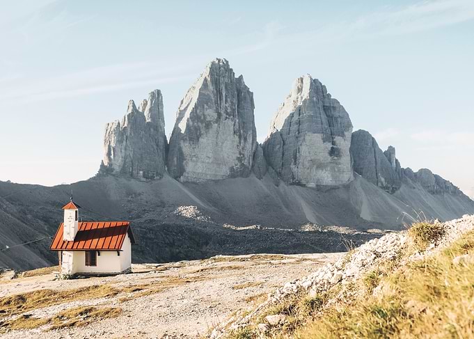 Dolomites, Italy I Isolated church in front of the Alps mountain peaks of the Tre Cime di Lavaredo for a panorama view of an imposing rock nature landscape in the pastel soft light of sunrise sunset