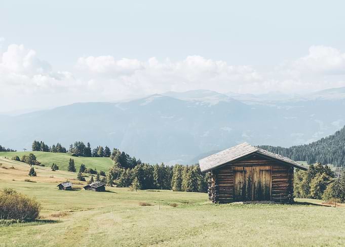 Dolomites, Italy I Picturesque wooden chalet in Alpe di Suisi with panorama skyline mountain views in its green meadow and fir trees with the retro vintage aesthetic of a pastel boho Italian summer