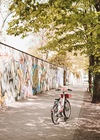 Berlin, Germany I Poetic springtime street scene with a bicycle by the Berlin Wall in pastel tones aesthetic urban greenery and colorful street art mural for a soft nostalgic atmosphere photography