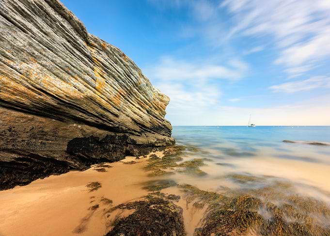 Coastal Rock Formation with Distant Sailboat