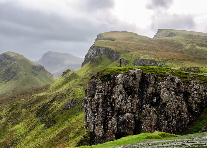 Person on Cliff Overlooking Green Hills