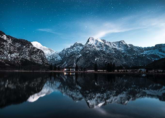 snowy mountains reflected in lake at night