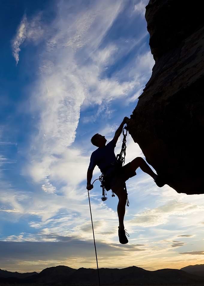 Silhouette of Rock Climber Against Cloudy Sky