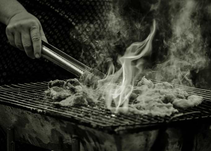 Grilling Meat with Tongs and Flames