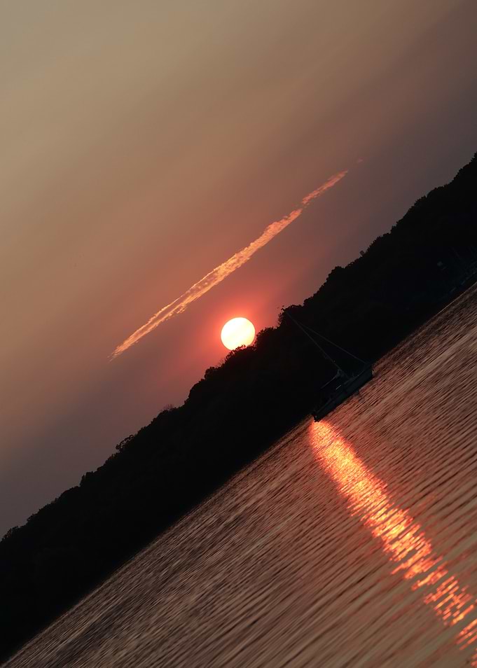 Sunset over water with sailboat silhouette