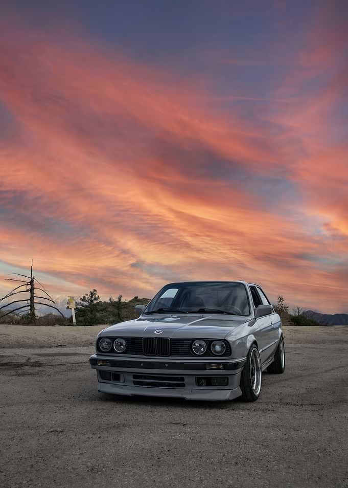 Gray BMW E30 under a sunset sky