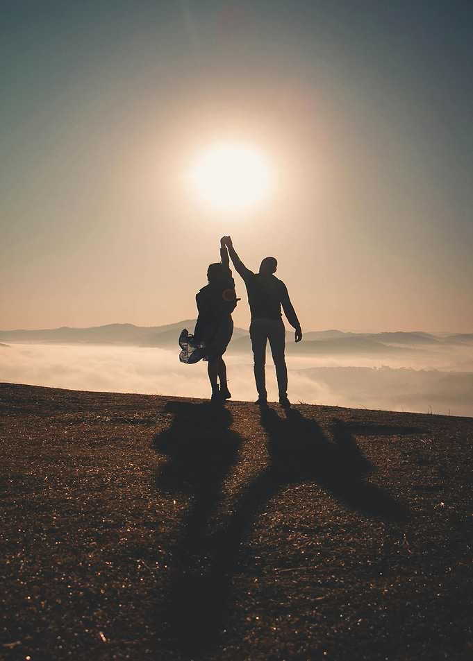 Silhouette of couple holding hands at sunrise