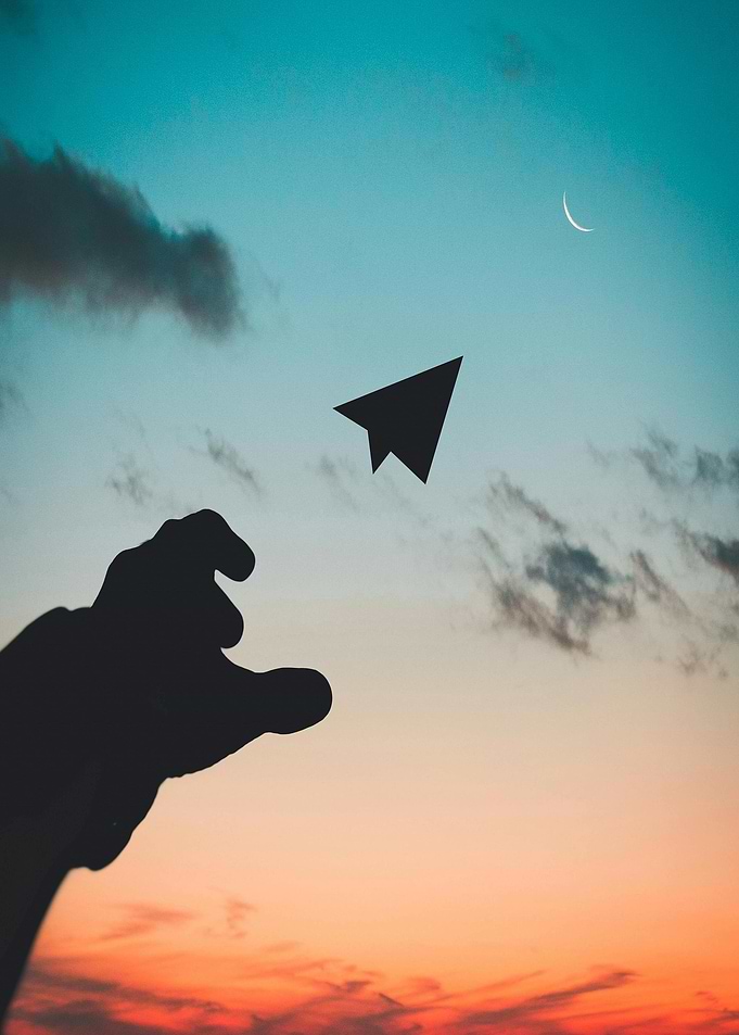 Paper airplane silhouette against sunset sky