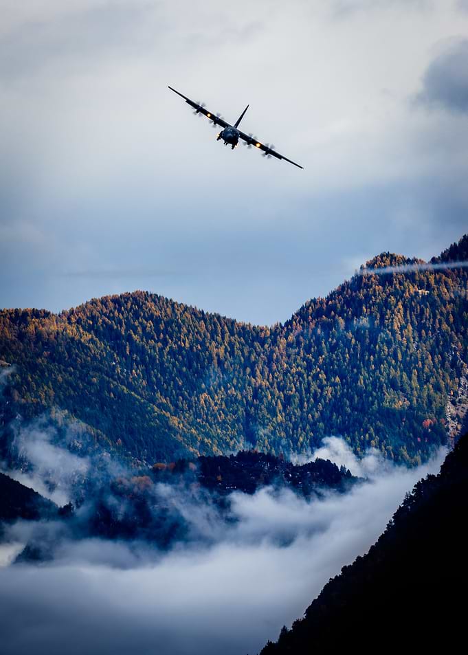 Danish C130 flying over misty mountains.