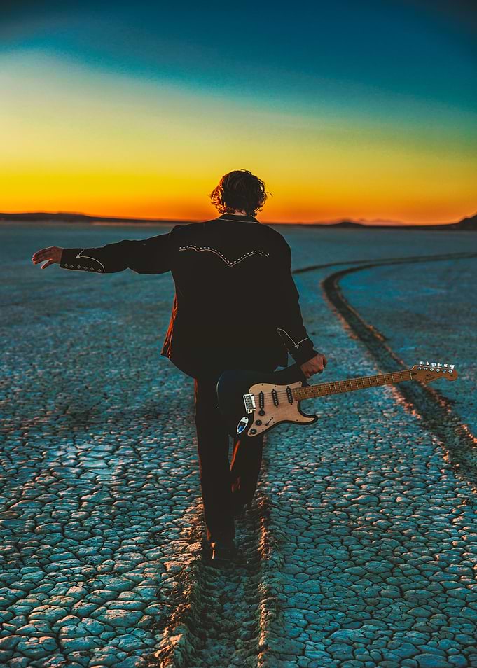 Guitarist walking in the desert at sunset
