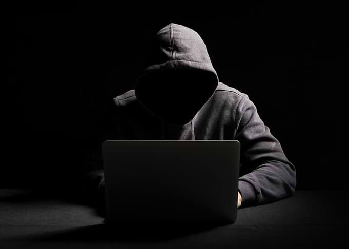 Hooded Figure with Laptop in Dark hacker hacking
