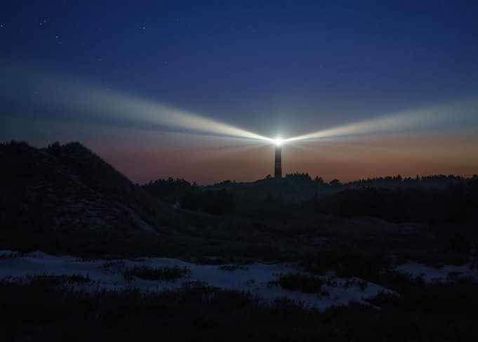 Amrum Lighthouse illuminating the night sky in the sand dunes