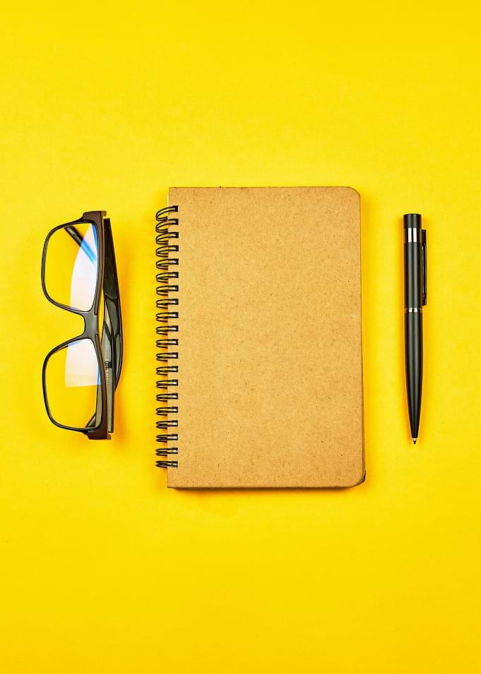 Notebook, Glasses, and Pen on Yellow Background