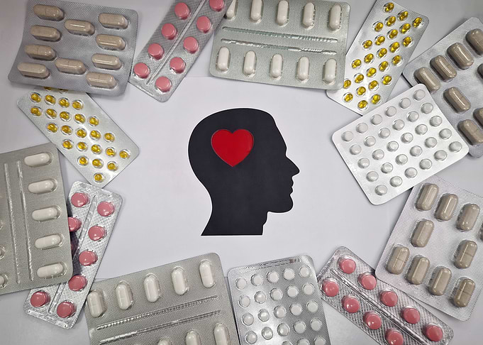 Pills surrounding a silhouette of a head with a heart
