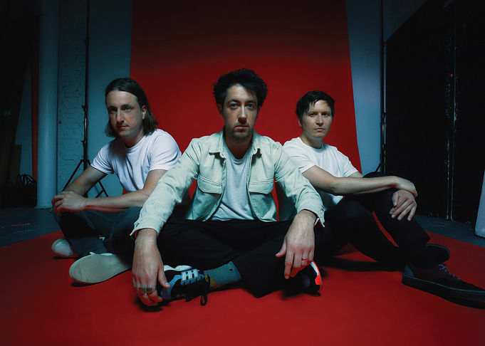 Three men sitting on red floor the wombats