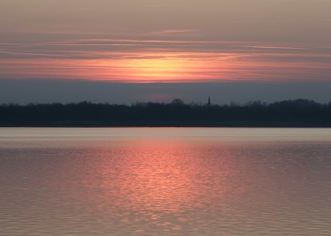 Sunset over a calm lake with a distant church spire