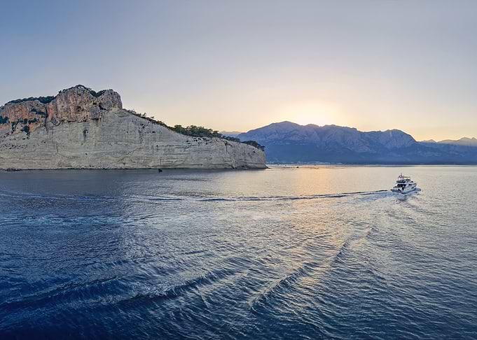 Yacht sailing by a cliff at sunset