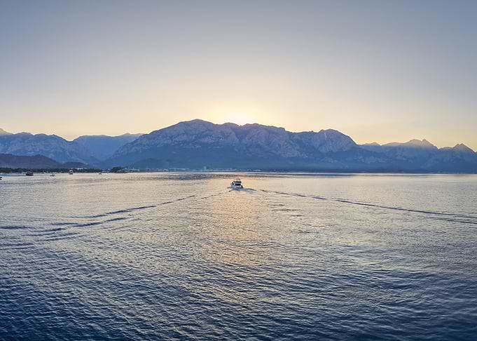 Boat sailing towards mountains at sunset