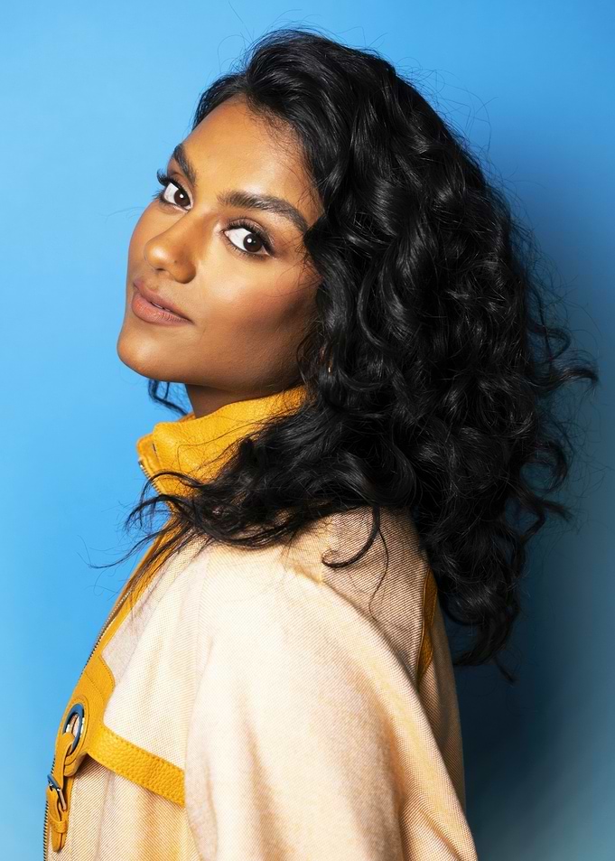 simone ashley in yellow jacket against blue background