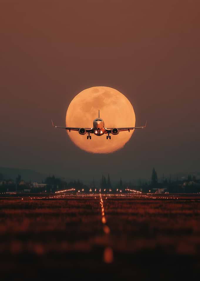Airplane flying in front of a large moon