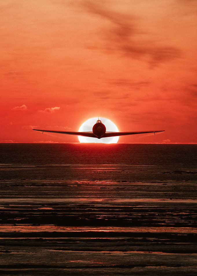 Airplane flying into the sunset over the ocean