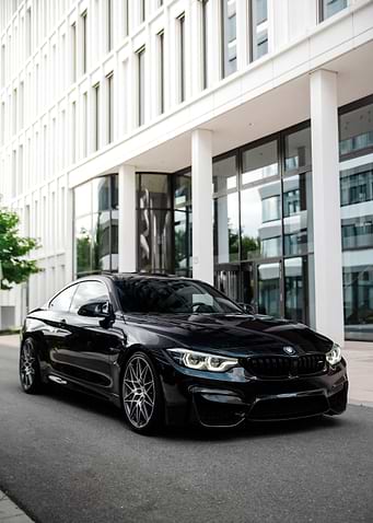 Black BMW M4 Coupe in front of modern building