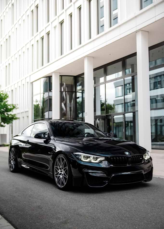 Black BMW M4 Coupe in front of modern building