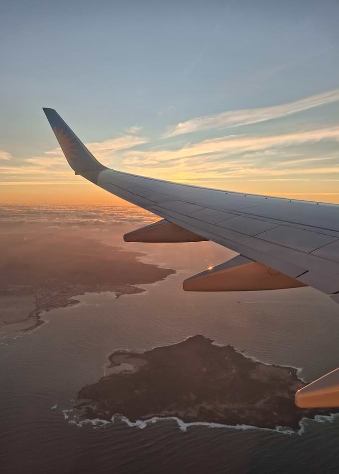 Airplane wing over coastal landscape at sunset