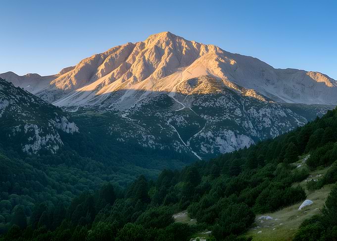Sunlit Mountain Peak Over Forest Valley